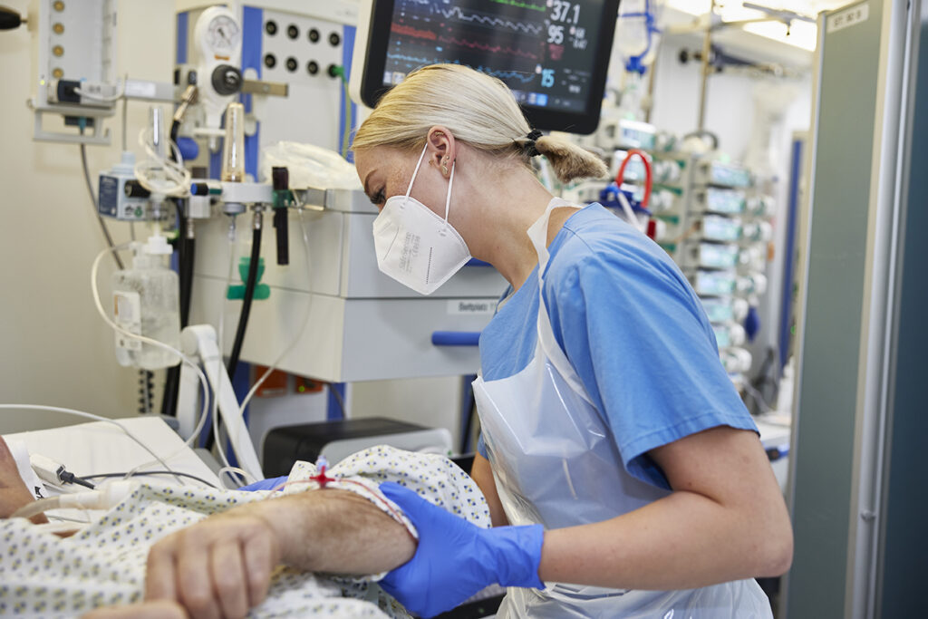 Pflegefachkraft mit Mundschutz am Krankenbett